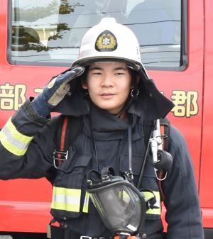 消防車を背景に防火衣を着て敬礼している中学生の写真
