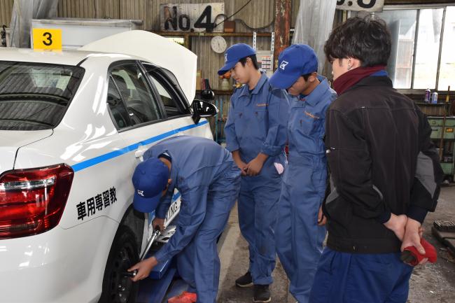 鴨川車検整備協業組合の職員が見守る中タイヤ交換を行う中学生たち