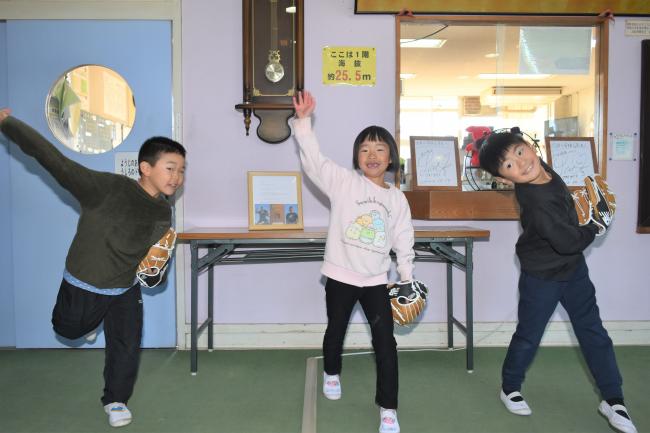 大谷選手から寄贈されたグローブをつけて記念撮影をする男子生徒2人と女子生徒1人