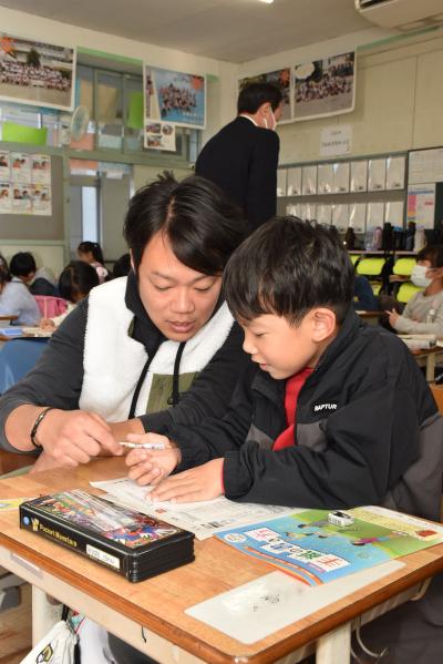 児童に年賀状の書き方を指導する担任教諭