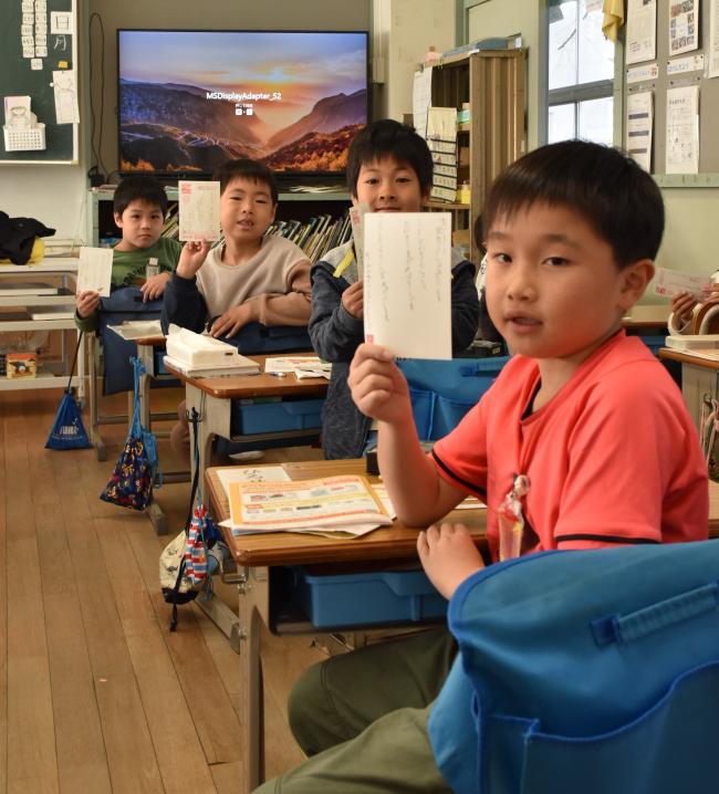 完成した年賀状を見せる男子児童