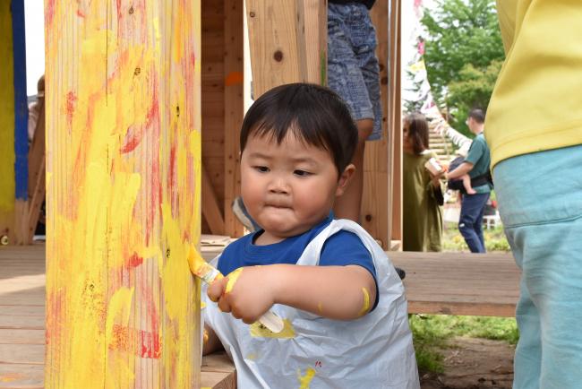 農園の小屋の柱にペンキを塗る男の子