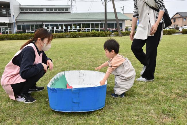 お弁当箱を模した大きな箱におかずのおもちゃをいれる子ども