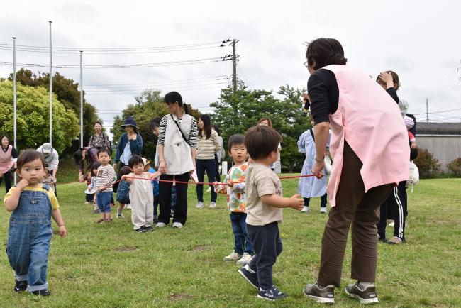 赤いロープをもって電車遊びをする子どもたち
