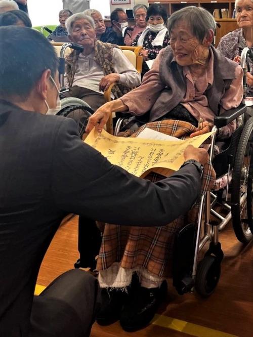 お祝い状を受け取られる永井初江さん、施設の皆さんと