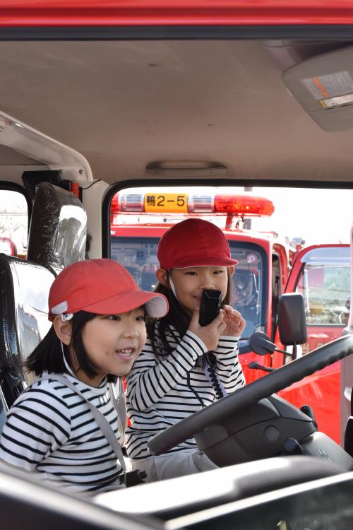 消防団車両(消防ポンプ車)体験搭乗し、無線を口元にｚてる児童