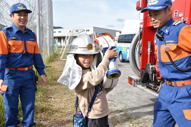 防火服を着て消防ホースをもった児童