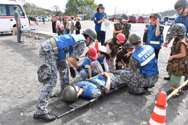 自衛隊の服をきて重傷者を運ぶ訓練を行う児童