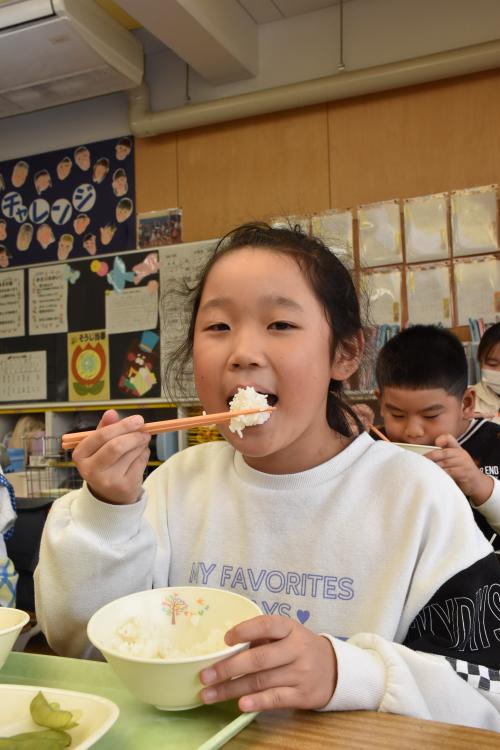 寄贈の新米長狭米をおいしそうにほおばる江見小学校２年の女の子の写真