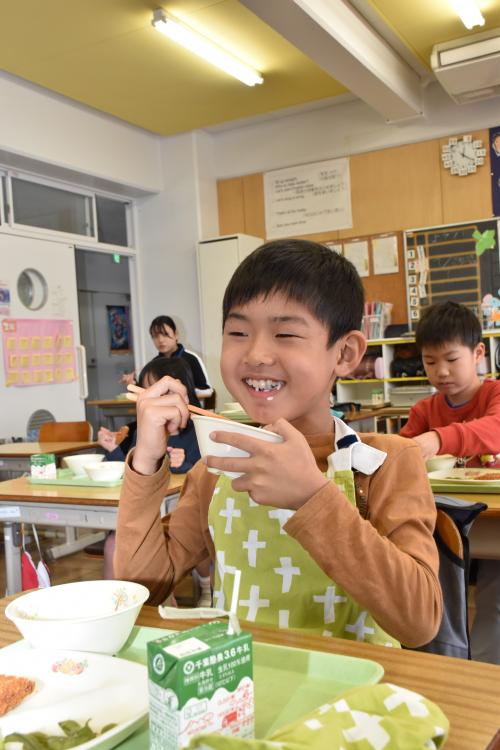 寄贈の新米長狭米をおいしそうにほおばる江見小学校２年生の男の子の写真