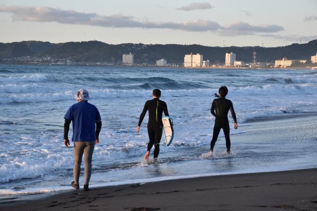 サーフボードをもって補助者と海へ向かう市長の写真