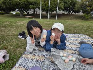 2人の子どもが色をつけた卵を寝転がりながら見せている