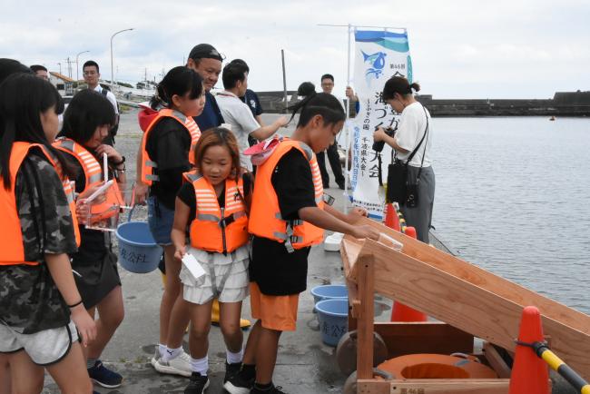 順番にマダイの稚魚を放流する児童の写真
