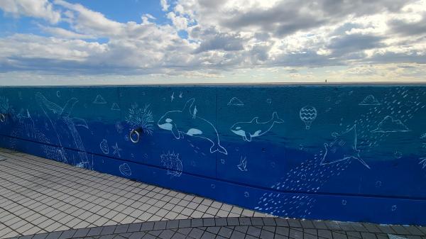青く海のように塗られた壁にシャチやクジラが泳ぐ姿が描かれたウォールアート